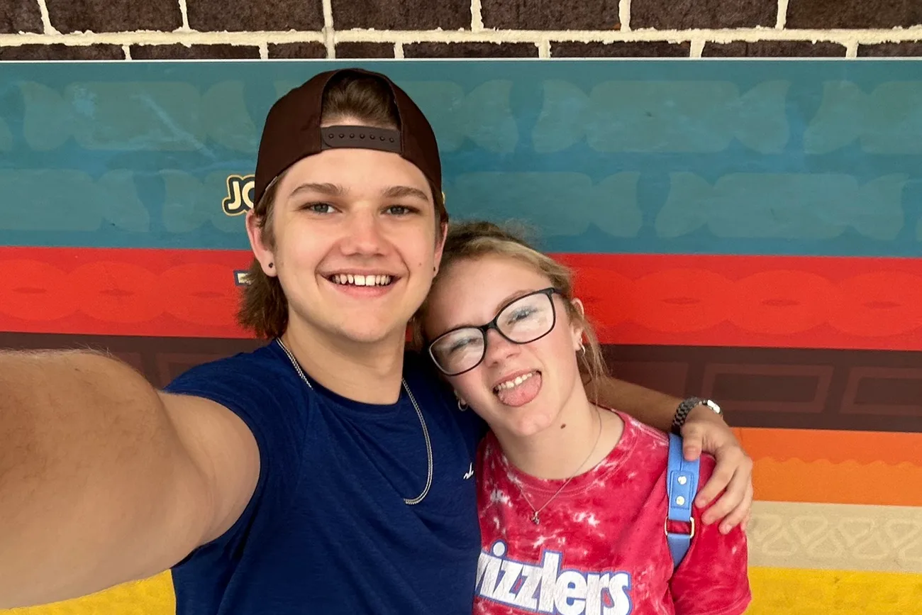Connor and the photographer in a selfie in front of a brick wall painted with colorful stripes